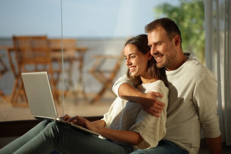 Couple using a laptop indoors, smiling and relaxing in a cozy home environment.