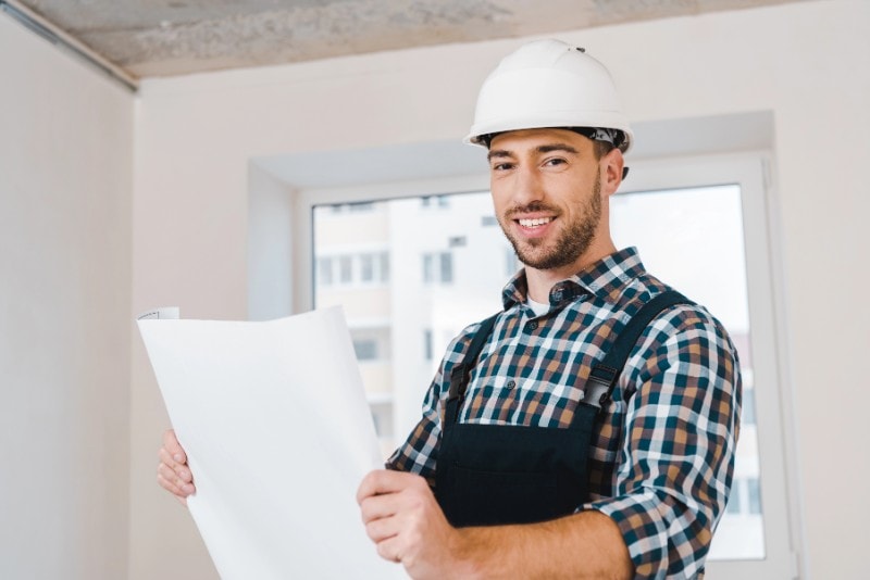 Skilled construction worker with a hard hat holding blueprints indoors.