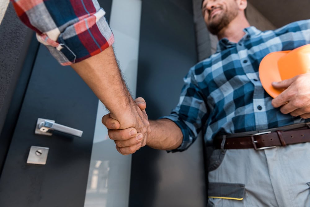 Handsome man in plaid shirt shaking hands with builder outside a house.