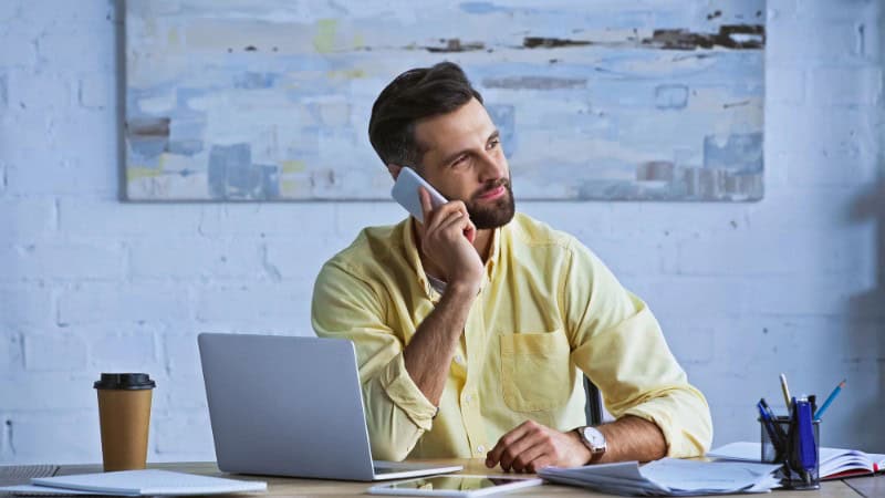 Man working at desk with laptop and phone in an office setting.