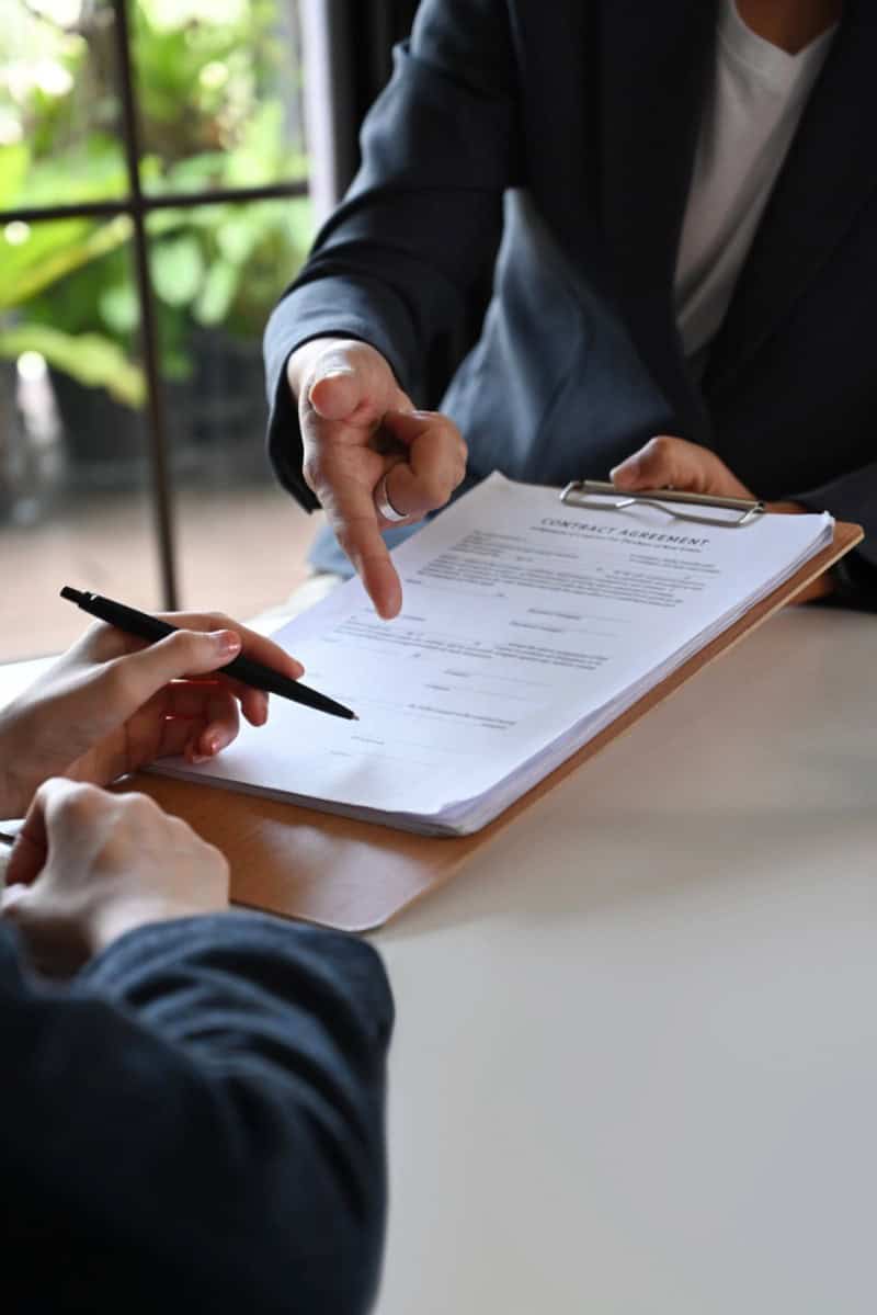Business professional signing contract with client in office setting.