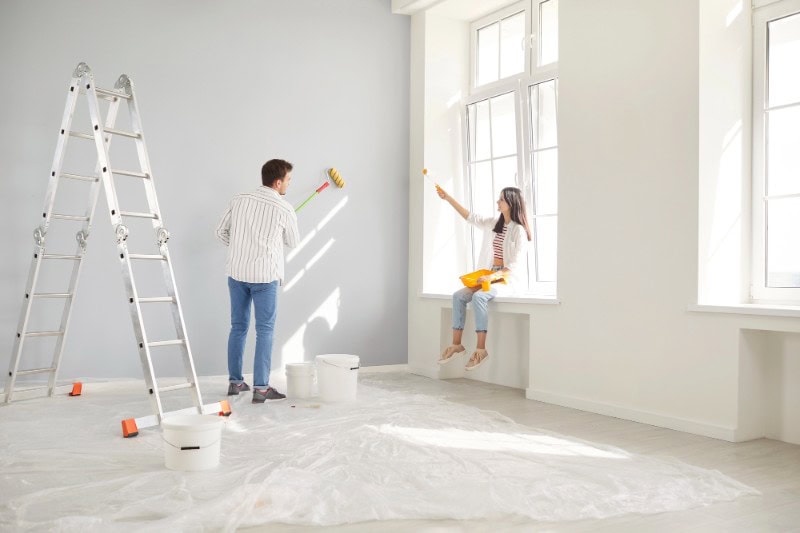Interior painting by Prolific Builders with two workers painting walls and preparing the space.