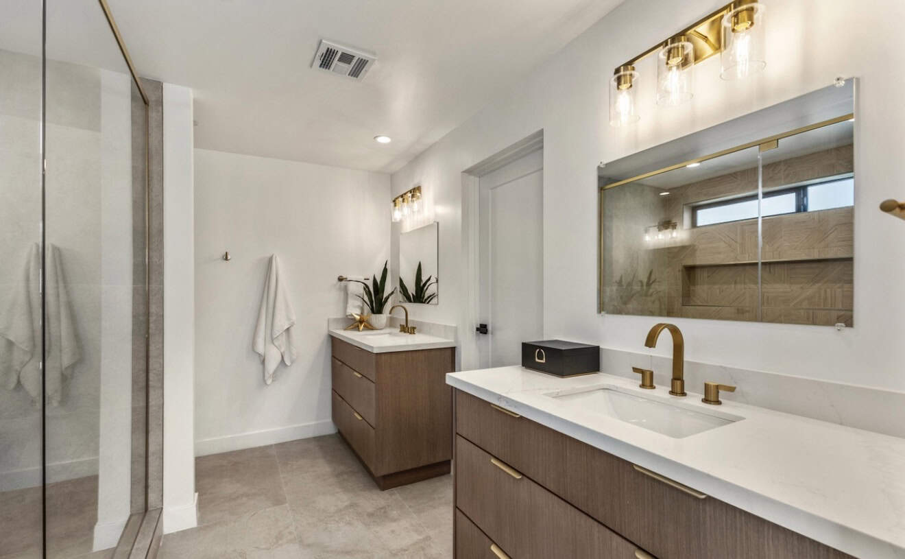 Contemporary bathroom featuring sleek vanity, gold fixtures, and large mirror.